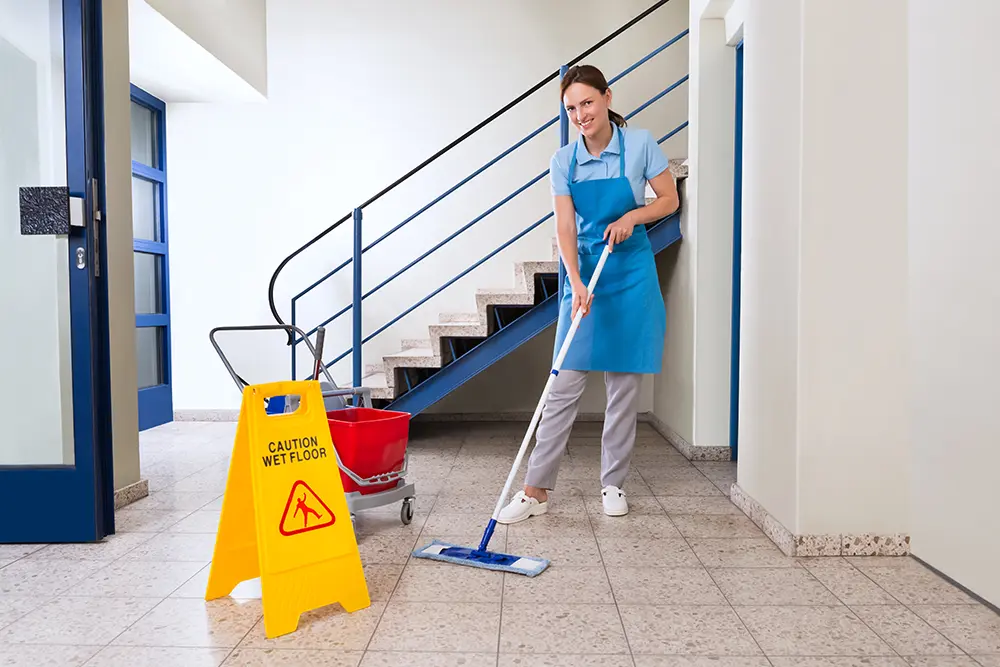 Arbeiter mit Reinigungsgeräten und Warnschild „Nasser Boden“ - Treppenhausreinigung - Hanover